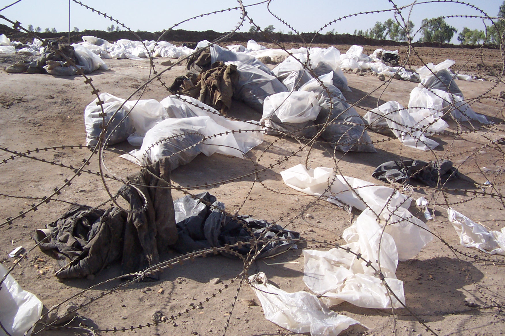In Tücher und Plastik gehüllte Überreste hinter Stacheldraht